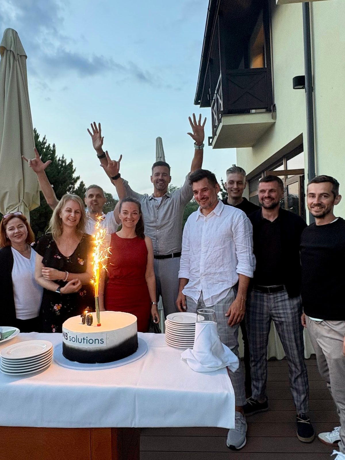 The MNB Solutions team celebrating around the anniversary cake with a sparkler